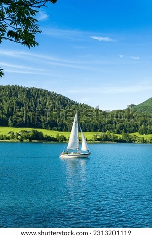 Sailing boat in the lake against the background of mountains and green forest. Sailboat floating on the water on a beautiful summer day with a clear blue sky. near St. Gilgen, Austria.  Royalty-Free Stock Photo #2313201119