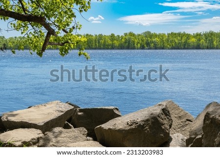 Wide Dnieper river (Dnipro) with stones and trees on the bank on a sunny spring or summer day