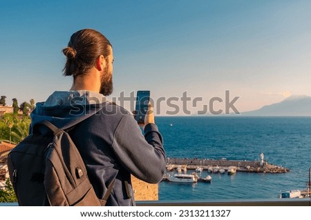 A man tourist takes a picture of the old port in the Turkish city of Antalya with his phone. A tourist takes a photo in the old district of Kaleiçi in Antalya.