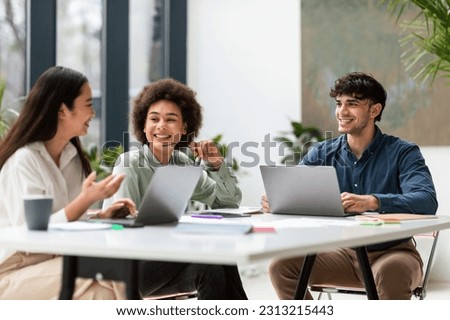 Office Productivity. Business Team Of Three Cheerful Multiracial Coworkers At Laptops Working And Discussing Projects At Workplace, Sitting At Desk Together Indoor. Corporate Teamwork Concept Royalty-Free Stock Photo #2313215443