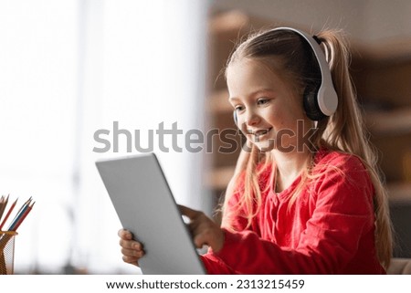 Smiling Little Girl Wearing Wireless Headphones Playing With Digital Tablet At Home, Happy Cute Preteen Female Child Browsing Games On Modern Gadget, Enjoying Online Gaming, Copy Space