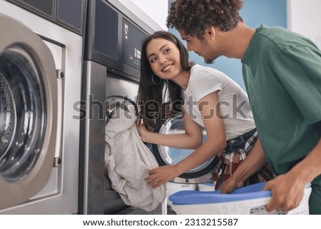 Happy Couple Folding Laundry Together At Laundromat Washing Machine Indoor, Smiling To Each Other Enjoying Convenience Service Together On Weekend. Spouses Washing Clothes At Public Laundrette Royalty-Free Stock Photo #2313215587