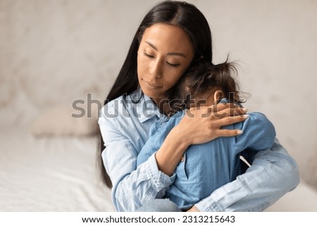 Baby Care. Japanese Mother Holding Child Daughter In A Loving Warm Hug, Snuggling And Hushing Little Toddler Girl In Cozy Bedroom Indoors. Mommy Caring For Infant At Home. Babysitting Concept
