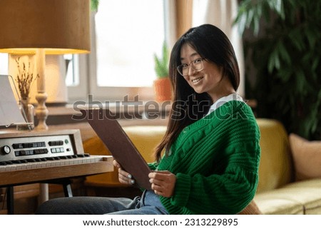 Smiling asian girl sitting near the piano at home