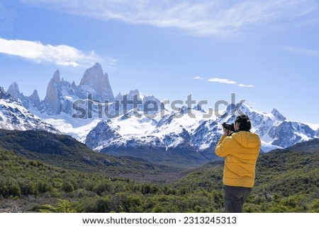man standing taking a picture of mount fitz roy in argentina's patagonia, wearing yellow jacket