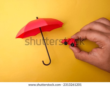 Hand holding red car covered by red umbrella on a yellow background