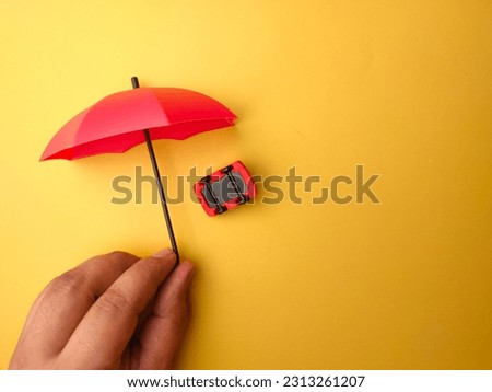 Hand holding red umbrella covered red car on a yellow background