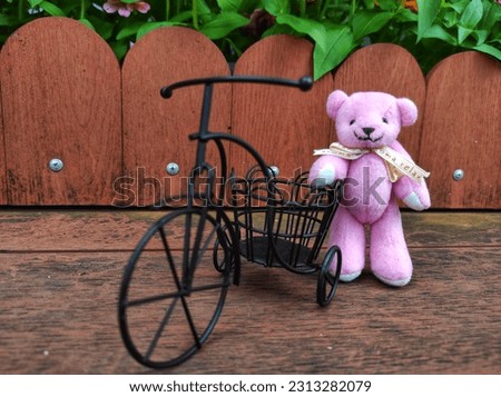 Pink mini Teddy Bear doll, decorative miniature bicycle on garden wooden planks background.