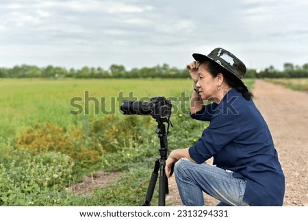 woman photographer sitting by her camera on tripod while waiting to shoot  in the middle of rice field