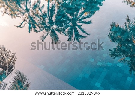 Palm trees reflection in swimming pool under sunset sunlight. Artistic summer leisure lifestyle concept. Calm bright water surface dream travel outdoor recreational background. Summer vacation closeup