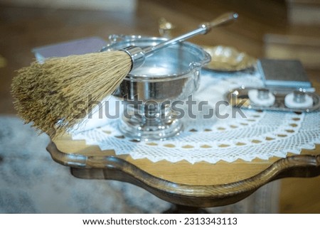 Liturgical vessels with holy water in the church. Broom for lighting in the church with holy water. Soft selective focus. Artificially created grain for the picture