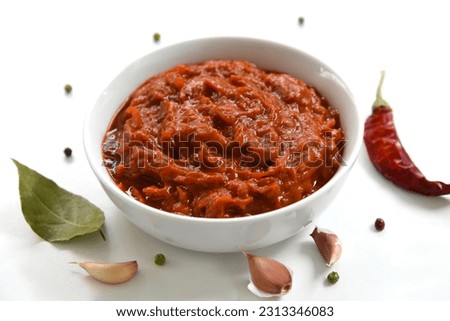 A bowl of red sauce, closeup, spices, and hot chili pepper. Homemade dip, relish, spicy spread. Bulgarian Lyutenitsa, or Balkan Ajvar, with tomato, eggplant, paprika, garlic. Traditional condiment. Royalty-Free Stock Photo #2313346083
