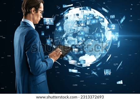 Side view of young european businessman using tablet with creative globe with telecommunication picture icons on blurry blue background. Business, video conference, remote group work