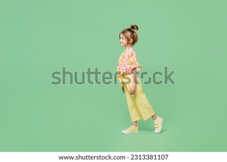 Full body side view smiling happy little child kid girl 6-7 years old wear casual clothes walk go isolated on plain pastel green background studio portrait. Mother's Day love family lifestyle concept Royalty-Free Stock Photo #2313381107