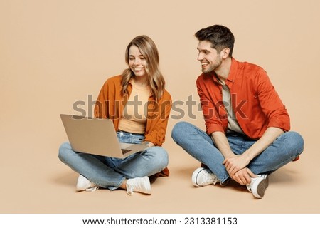 Full body young couple two friends family IT man woman wear casual clothes together sitting hold use work on laptop pc computer isolated on pastel plain light beige color background studio portrait