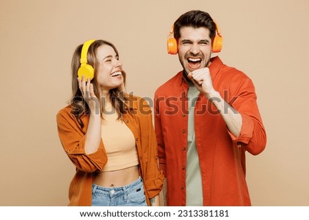 Young fun couple two friends family man woman wear casual clothes headphones listen music sing song in microphone looking camera together isolated on pastel plain light beige color background studio