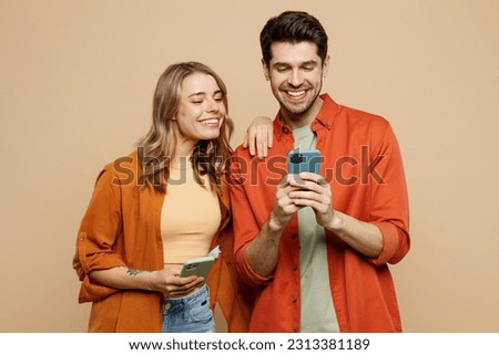 Young smiling happy couple two friends family man woman wear casual clothes hold in hand use mobile cell phone together chatting isolated on pastel plain light beige color background studio portrait Royalty-Free Stock Photo #2313381189