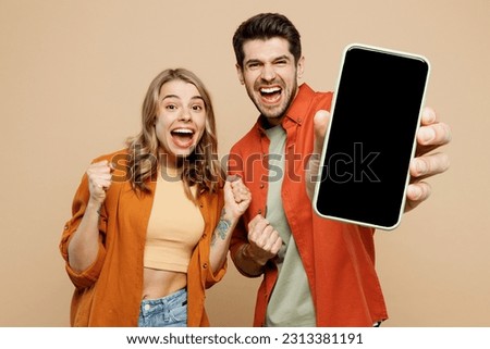 Young couple two friends family man woman wear casual clothes hold in hand use mobile cell phone with blank screen workspace area do winner gesture together isolated on pastel plain beige background