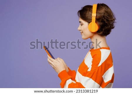 Side view young cheerful woman she wear casual clothes sweatshirt headphones listen to music use mobile cell phone isolated on plain pastel light purple background studio portrait. Lifestyle concept