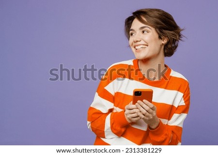Young fun woman she wear casual clothes sweatshirt hold in hand use mobile cell phone brwosing internet look aside on area isolated on plain pastel light purple background studio. Lifestyle concept