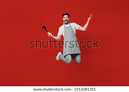Full body surprised excited fun young male housewife housekeeper chef cook baker man wear grey apron hold in hand soup black ladle dipper isolated on plain red background studio. Cooking food concept