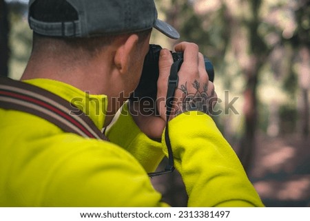 Young photographer with hat working taking capture photo of nature in the woods holding and using his camera in autumn or winter time