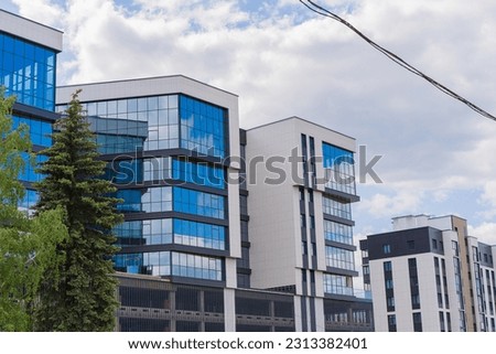 Modern Glass Tower with Stunning Blue windows and White Clouds reflections of the Sky near a green trees
