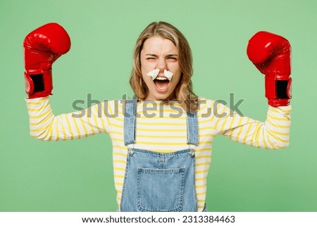 Sick unhealthy ill allergic strong woman has red watery eye runny stuffy sore nose with tissue suffer from allergy trigger symptom hay fever wear boxing gloves fight isolated on plain green background Royalty-Free Stock Photo #2313384463