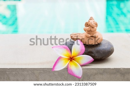 Clay Ganesh sculpture on stone with beautiful plumeria flower over blurred water background, outdoor day light, peaceful and happiness concept Royalty-Free Stock Photo #2313387509