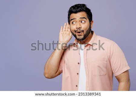 Young curious nosy Indian man he wears pink shirt white t-shirt casual clothes try to hear you overhear listening intently isolated on plain pastel light purple background studio. Lifestyle concept Royalty-Free Stock Photo #2313389341