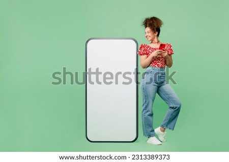 Full body young woman she wearing casual clothes red blouse big huge blank screen mobile cell phone smartphone with area using mobile cell phone isolated on plain pastel light green color background