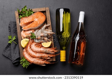 A top view of fresh seafood such as shrimp, langoustines, and trout steaks, accompanied by white and rose wine Royalty-Free Stock Photo #2313390119