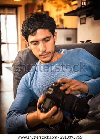 Young male photographer holding and looking at his photocamera
