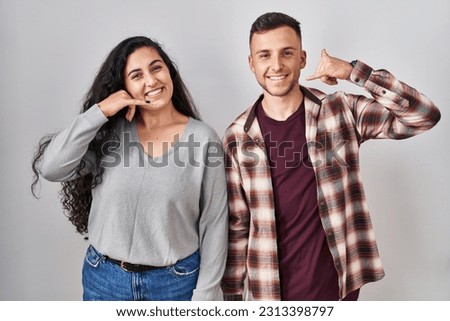 Young hispanic couple standing over white background smiling doing phone gesture with hand and fingers like talking on the telephone. communicating concepts. 