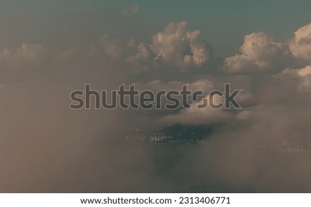 a dreamy photo at Bird's-eye view of the sea and coastal town shrouded by a low lying layer sea clouds under a hazy blue sky and cloud clusters