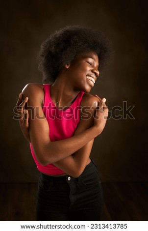 a young black woman with afro hair and a big smile embraces with happiness