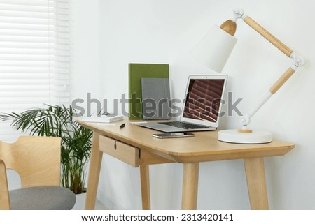 Cozy workspace with laptop, smartphone and lamp on wooden desk at home