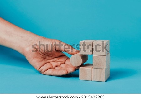 a man is putting a cylindrical building block in a stack of rectangular building blocks, on a blue background Royalty-Free Stock Photo #2313422903