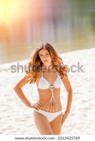 Portrait of a stunning beautiful young girl in a white bikini on the beach. Background sand, blurred bokeh sea and sun rays. Beauty and fashion for summer concept