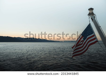 A scenic shot of mountain silhouettes across the sea with the American flag waving on a pole