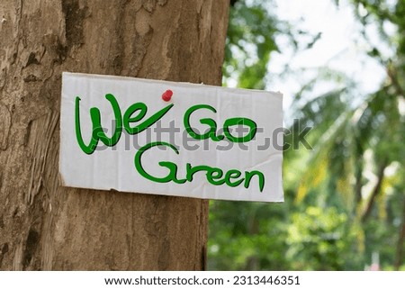 Cardboard from boxes cover with heart drawing and texts 'We Go Green', was sticked on tree bark to call out all people to care about and to beat the pollution from plastic and reduce global warming.