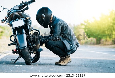 Biker repairing motorcycle on the road. Motocyclist fixing the motorcycle on the road, Man checking his motorcycle on the road Royalty-Free Stock Photo #2313451139