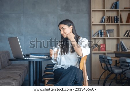 Young woman with a glass of water in front of a laptop, the concept of studying remotely.