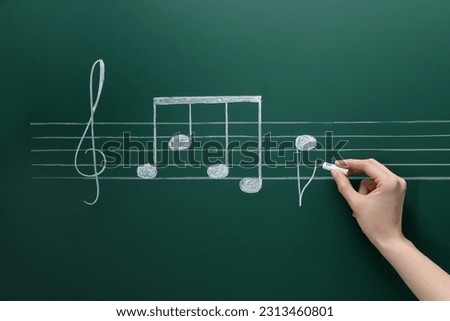 Woman writing musical notes with chalk on blackboard, closeup