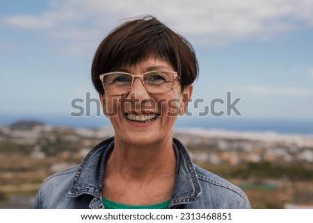 Happy senior woman smiling on camera at house rooftop with ocean view in the background - Joyful elderly concept