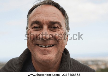 Happy senior man smiling on camera at house rooftop with ocean view in the background