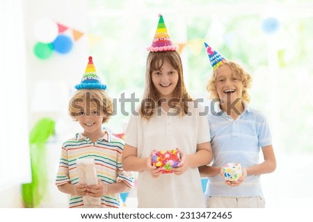 Kids birthday party. Children play with balloons and open presents. Little girl and boy dance and jump. Blowing birthday cake candles and opening gifts. Decoration for fun themed event celebration.