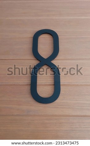 Block number eight on a brown wooden wall background. Numeric sign or symbol. Number 8 eight  black acrylic on wooden isolated. 