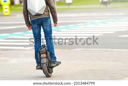 Man on electric monowheel (EUC). Stylish guy moves along sidewalk on mono wheel. Man cross road on electric unicycle, commuting to work. Portable individual transportation vehicle.  Royalty-Free Stock Photo #2313484799