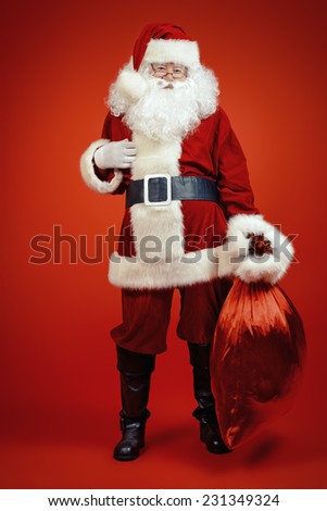 Santa Claus comes with a big bag of gifts. Full length portrait.